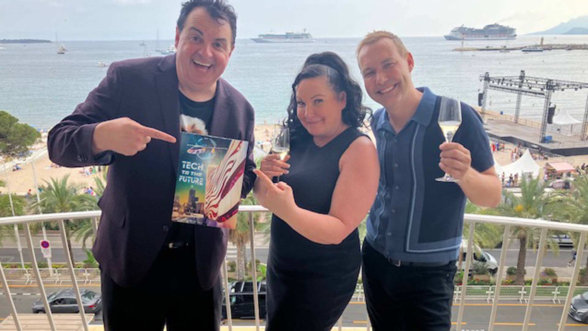 Three people on a seafront terrace, one holding a Tech To The Future leaflet.